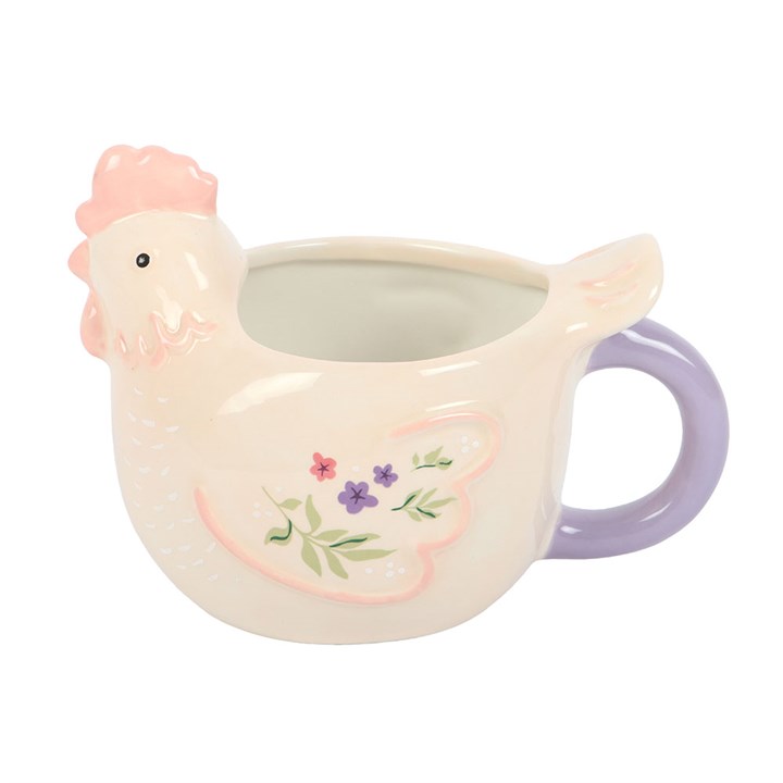 Side view of a sculpted cream ceramic mug shaped like a hen with a pink comb and lilac handle, featuring pastel floral paintings on its wings, on a white background.