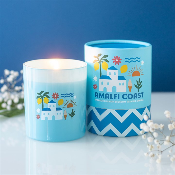Sky blue frosted glass candle featuring white villa and lemon illustrations, sitting next to a matching blue and white chevron gift tube