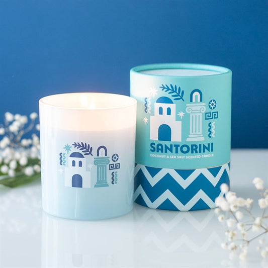 White frosted glass candle with Santorini church illustrations next to a light blue and white gift tube.