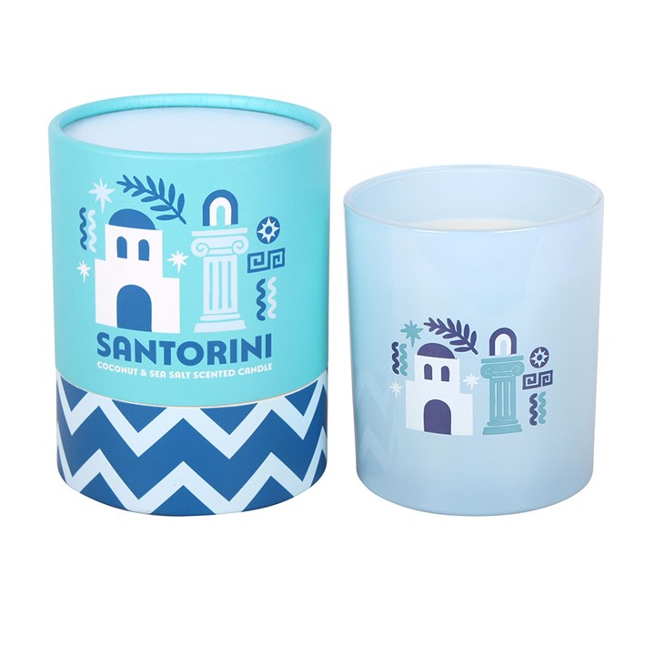 white frosted glass candle with Santorini church illustrations next to a light blue and white  gift tube on a white background