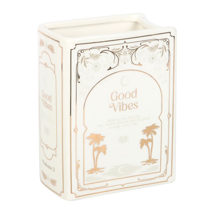 White ceramic vase shaped like an upright book with gold illustrations of palm trees and 'Good Vibes Volume 2' printed on the spine. on white background