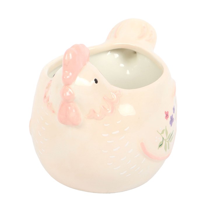 close up of front face of a sculpted cream ceramic mug shaped like a hen with a pink comb featuring pastel floral paintings on its wings on a white background