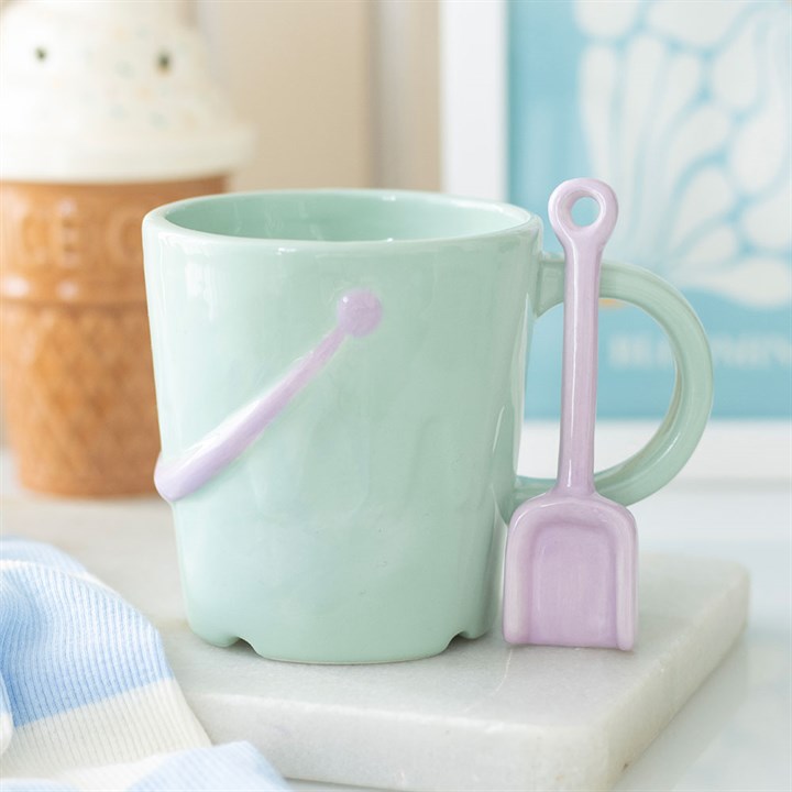 Mint green bucket-shaped ceramic mug with a matching lilac spade spoon sitting on a white marble coaster.