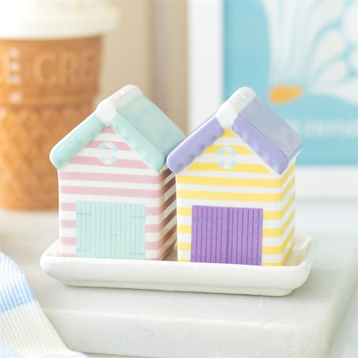 Two pastel-striped ceramic beach hut salt and pepper shakers in pink, yellow, and blue, sitting on a small white ceramic tray.