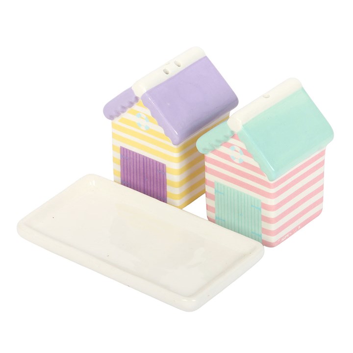 Two pastel-striped ceramic beach hut salt and pepper shakers in pink, yellow, and blue sitting beside a small white ceramic tray on white background