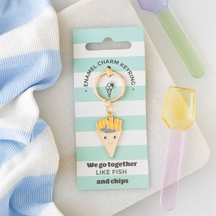 Enamel fish and chips cone keyring on a mint and white striped gift card that says 'We go together like FISH and chips', next to pastel dessert spoons."