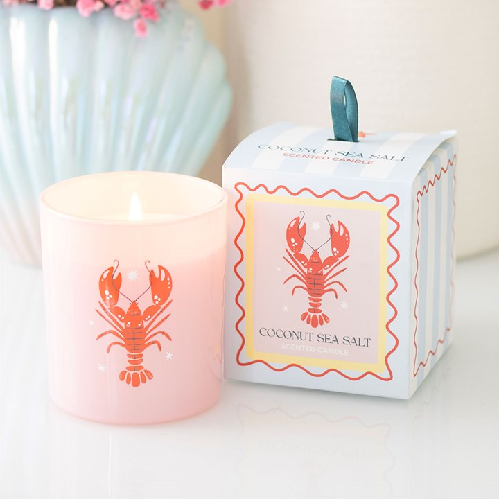 Pastel pink glass candle with red lobster illustration next to a blue and white striped gift box.