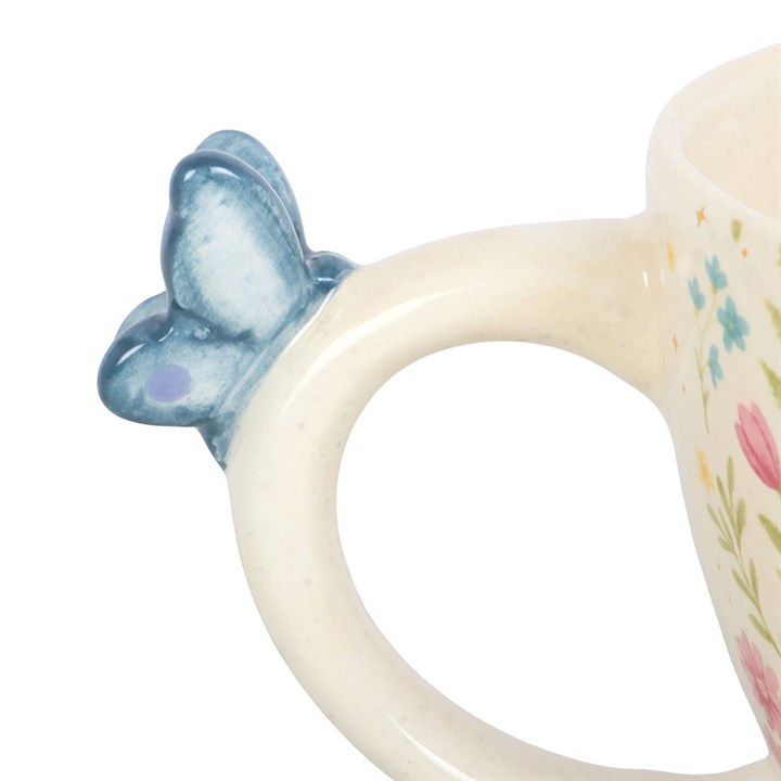 Close up of the 3D blue butterfly perched on the handle of a white ceramic mug handle on a white background.