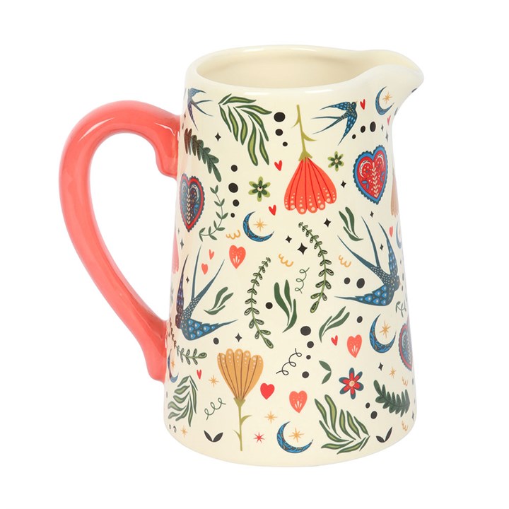 Cream ceramic jug with a red handle, covered in a colorful folk art print of wildflowers and birds on a white background