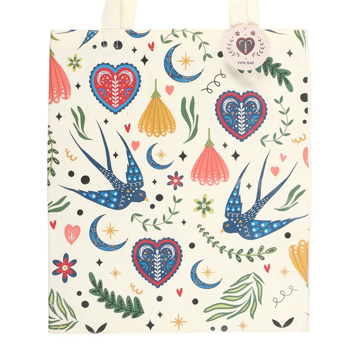Close up of Cream canvas polycotton tote bag covered in a colorful folk art print of blue swallows,flowers and hearts on a white background. 