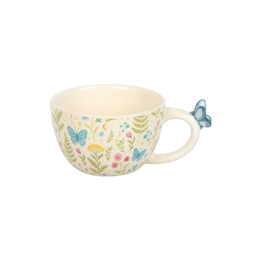 A wide white ceramic mug with a full-wrap print of pastel wildflowers and ferns, featuring a small 3D blue ceramic butterfly sculpted onto the handle, on a white background.